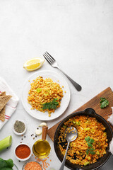Red lentils dal in black pan and on plate on white table top. Lentils carrot and lettuce vegetarian meal, top vertical view, copy space