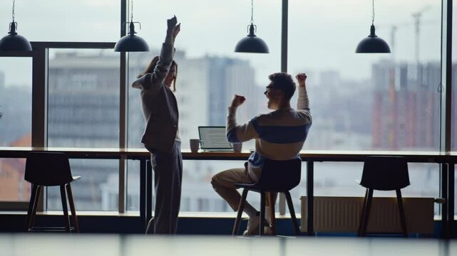 Emotional teammates watching computer celebrating victory in contemporary office