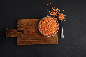 Red lentils on a ceramic plate on a wooden board on a black table, close-up, top view.