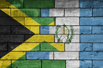 colourful painted big national flag of jamaica and flag of guatemala on a massive old brick wall background. concept