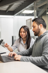 Two coworkers looking at a laptop, collaborating in a modern office. A casual work environment with focus and teamwork.

