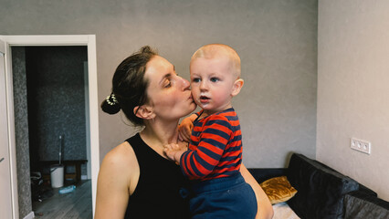 A loving mother feeds her little son with a spoon as they sit together in a cozy kitchen.