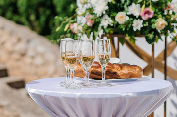 Elegant Wedding Celebration Table with Champagne Glasses, Bread, Flowers, and Floral Arch, Soft Pastel Tones, Outdoor Ceremony
