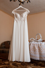 Elegant White Wedding Dress Hanging on Hanger, Bridal Gown, Peach Room, Lace Details, Formal Event, Luxurious Style, Feminine Fashion