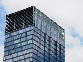 Fototapeta premium Modern glass skyscraper office building facade with reflective windows against blue sky and white clouds