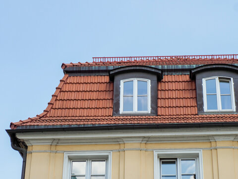 Historic European house with distinctive mansard roof featuring dormer windows against bright blue summer sky
