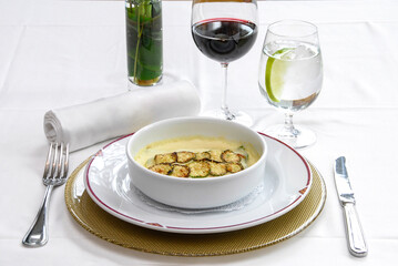 Zucchini soup, cream of zucchini served at a restaurant table, accompanied by a glass of red wine and fresh lemonade.