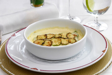Zucchini soup, cream of zucchini served at a restaurant table, accompanied by a glass of red wine and fresh lemonade.