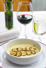 Zucchini soup, cream of zucchini served at a restaurant table, accompanied by a glass of red wine and fresh lemonade.