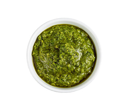 A white ceramic bowl filled with vibrant green pesto sauce, textured with basil on transparent background