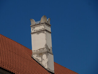 White stone chimney against orange clay roof tiles and clear blue sky background