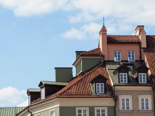 Historic European building with traditional red tile roof and dormer windows against blue sky