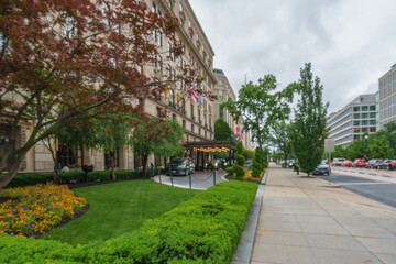 Naklejka premium Blurred view of a luxury hotel with formal gardens and flag-lined facade on a busy city street.