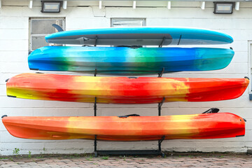 Paddle board and three kayaks stacked against a white block building.