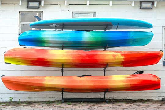 Paddle board and three kayaks stacked against a white block building.