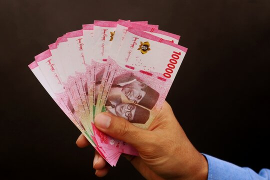 Businessman's hand holding 100,000 rupiah bill on dark background