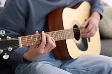 Fototapeta premium Young man playing guitar on sofa indoors, closeup