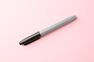One black marker on light pink background, top view