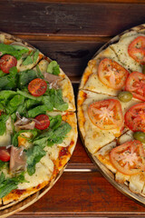 Dos pizzas con queso, coloridas, con tomates, servidas sobre una mesa de madera