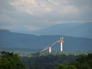The Olympic Jumping Complex in Lake Placid, Upstate New York, lit by late evening sun rays, seen from afar with mountains in the background.