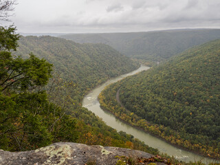 Covered in early fall colors, the mountains at New River Gorge extend towards the horizon, framed by rocks in the foreground and drifting clouds above.