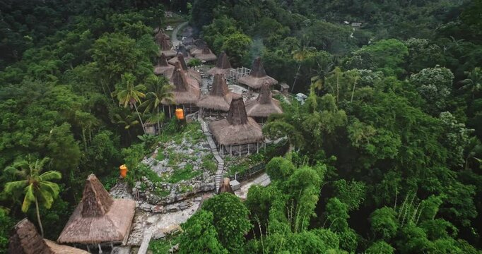 Aerial drone footage revealing traditional houses with conical roofs nestled in the lush tropical landscape of Sumba island, Indonesia, highlighting rich cultural heritage and unique architecture