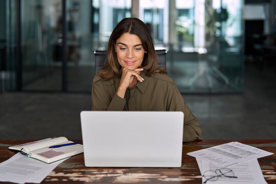 Smiling busy mature middle aged professional business woman, female company manager executive or entrepreneur looking at laptop computer in office working on online financial data sitting at desk.