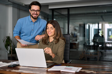 Two happy busy professional business people using laptop technology working together in office....