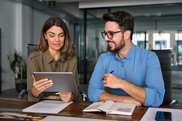 Plakat Middle aged female executive manager talking to male colleague having conversation sitting at workplace. Two busy happy professional business people working in office with digital tablet.