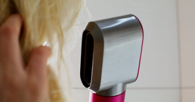 A woman dries her wet hair with a hair dryer. Close-up of a styler and her hair, unrecognizable person