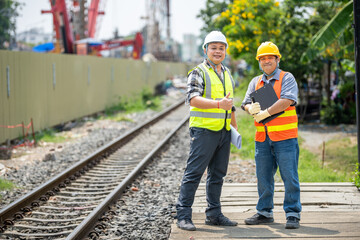 Two construction workers wea safety helmets and reflective vests standing outdoors at a...