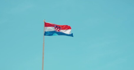Croatian national flag waving proudly on a pole against a bright clear blue sky - Powered by Adobe