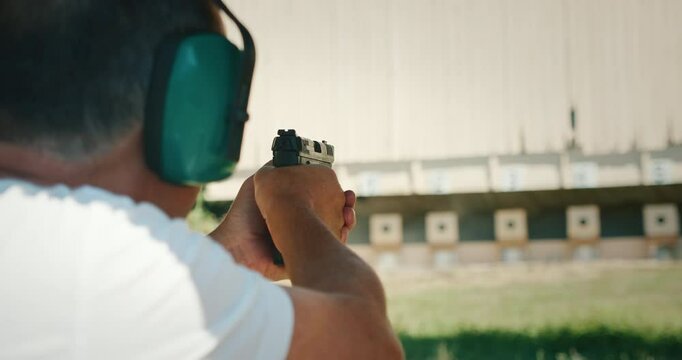 Older man with ear protection aiming a handgun at shooting range targets