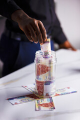 Black person putting Egyptian pound note in transparent plastic container containing more bank notes. savings concept vertical portrait mode format
