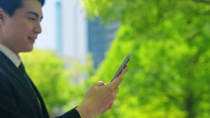 新緑の街でスマホを使う男性ビジネスパーソン - Powered by Adobe