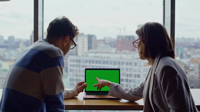 Two employees working chroma key device pointing screen in glass walls office