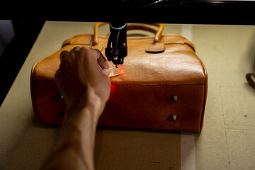 Obraz premium The process of making laser engraving on brown leather bags, perfect for leather industry company profile designs