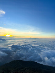 A breathtaking sunrise view above the sea of mist. Vibrant orange and purple hues light up the sky, with mist rolling over lush mountain peaks