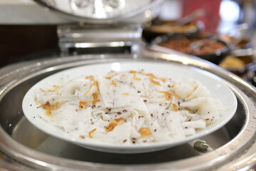 Vietnamese streamed rice rolls or banh cuon making by chef of restaurant in kitchen, rice flour liquid solidify by steam, then add filling and roll, delicious street food with simple 