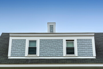 Two white-framed windows on house shed dormer under clear blue sky in Brighton, Massachusetts, USA