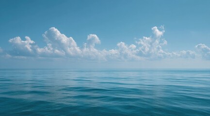Obraz premium Calm ocean scene with a horizontal line of fluffy white cumulus clouds against a clear, light blue sky
