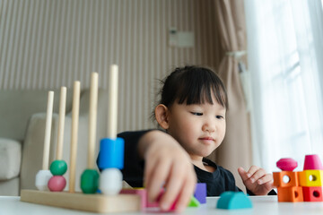 3 year old girl having fun playing with colorful geometric shape wooden blocks educational toys at...