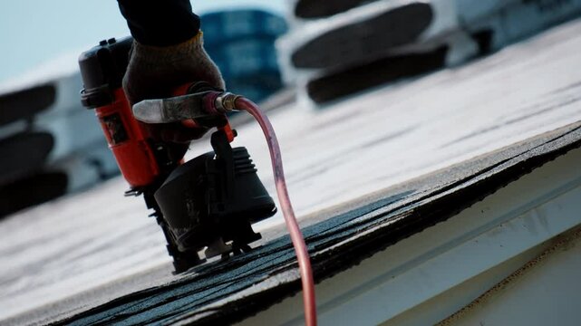 Roofer is nailing down shingles on the roof of residential house. Element of roof renovation
