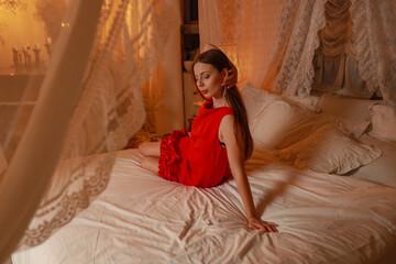 Obraz premium Young slim pretty brunette woman in red dress lying on bed in vintage bedroom
