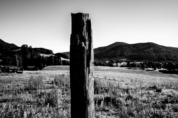 Old wooden fence post in countryside with mountains in the background in black and white