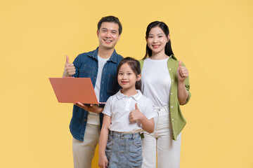 Obraz premium Happy family portrait with parents and daughter giving thumbs up with laptop against yellow backdrop