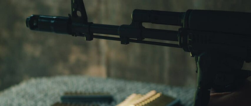Rifle fires outdoors as muzzle flash bursts from barrel above ground mat with bullets in foreground