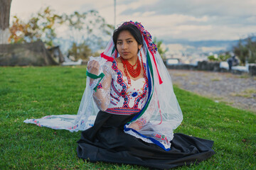 Indigenous woman wearing traditional dress and veil sitting on grass