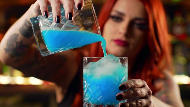 Person pouring a blue cocktail into a glass with ice