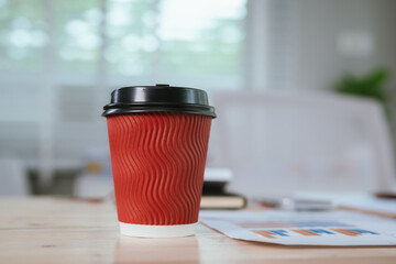 A warm cappuccino in a disposable paper cup with a plastic lid sits on a café desk, ready for take-away enjoyment.